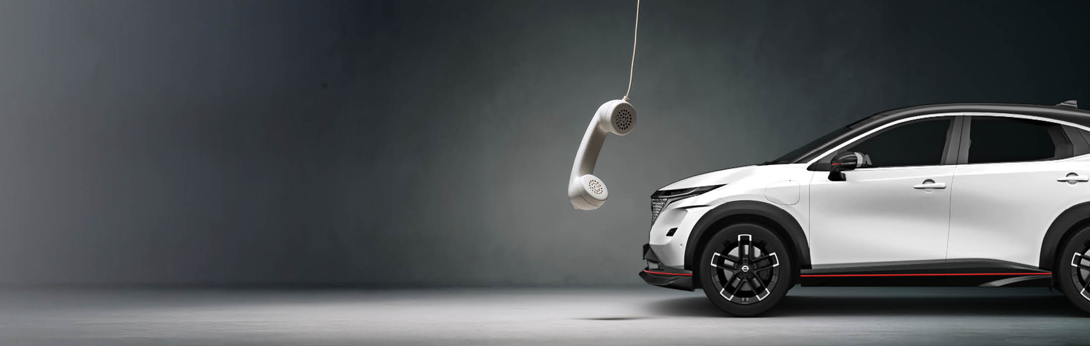 Ein weißes Auto steht schräg im Bild, davor hängt ein klassischer Telefonhörer von der Decke herab – Symbol für Erreichbarkeit und Kundenservice im Autohaus.